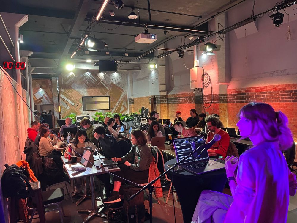 A venue full of people at their laptops and a close up of a speaker back-lit by purple light. 
