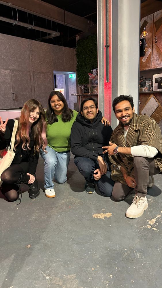Two women and two men crouching and positing for the camera while smiling. They're at a hip venue where you can see the coffee bar in the background.  