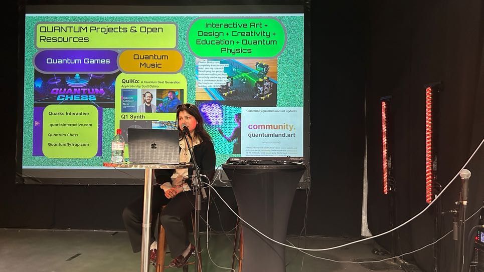 A woman sat behind a laptop presenting on a big screen. The screen reads: 'Quantum projects and open resources'
