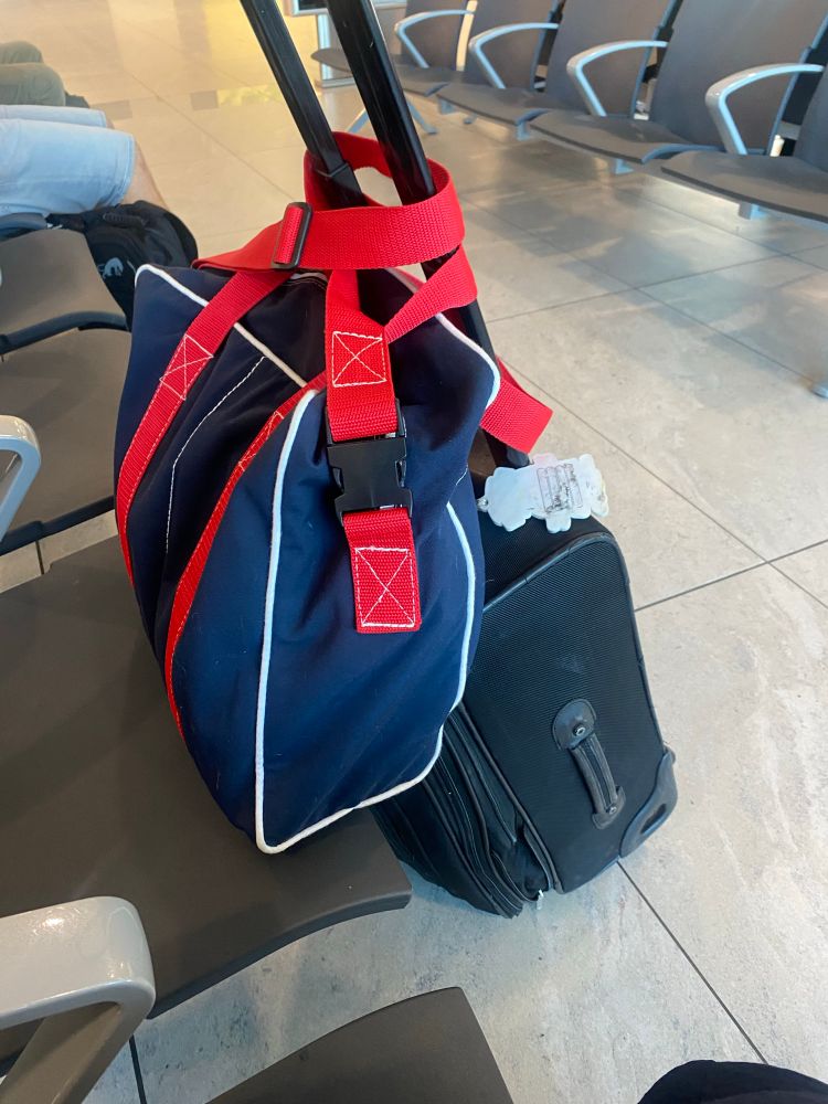 Black carry on suitcase topped by an equivalent sized navy blue canvas bag with red straps. 