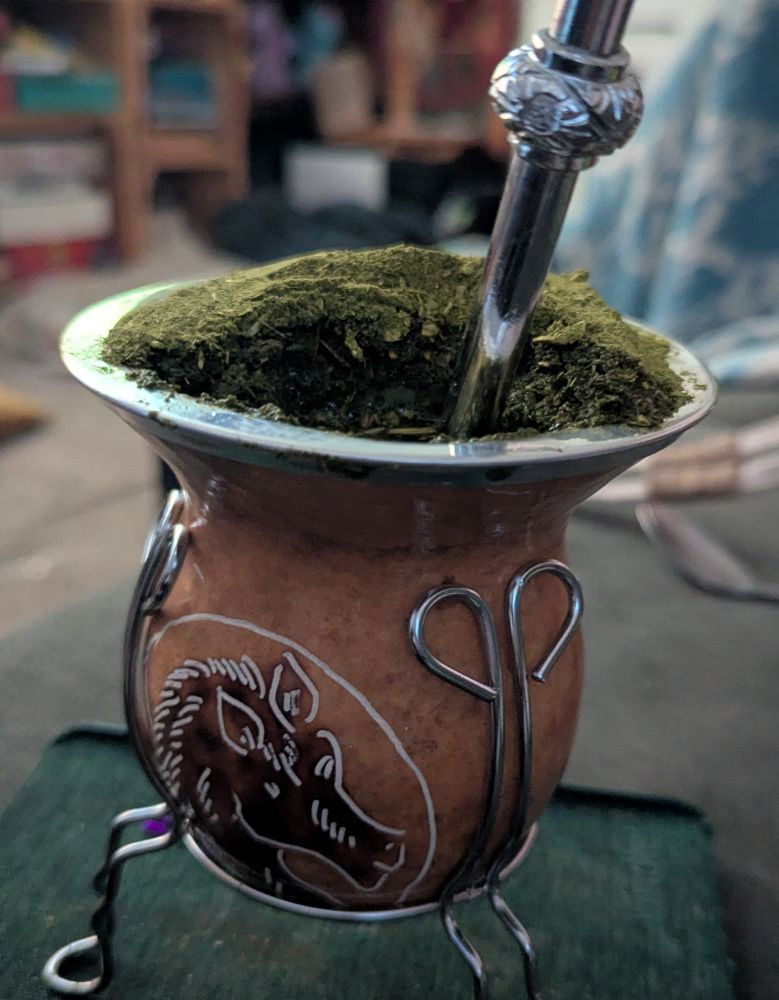 Hourglass shaped small gourd with a horse head carved in it. A mountain of fine green yerba maté sitting on top. 