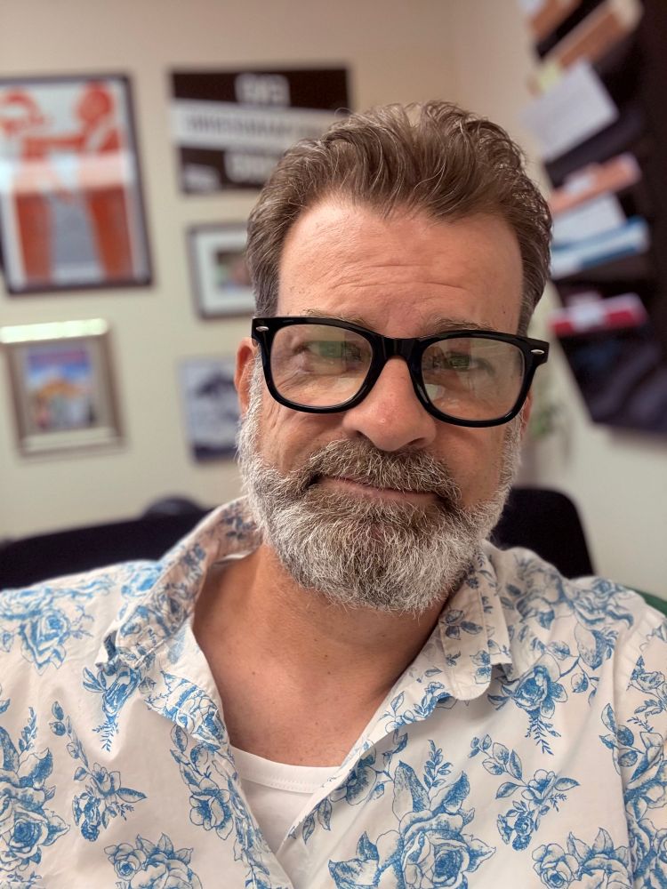 Selfie of the poster. 54 year old Caucasian male, brown hair, greying beard. Black rimmed glasses, white shirt with blue roses. 