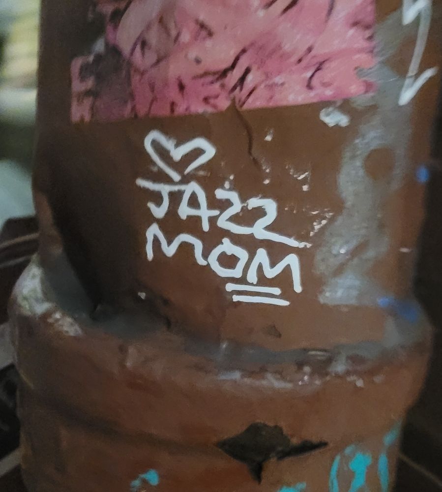 A pole outside with the words "JAZZ MOM" written in a paint pen.