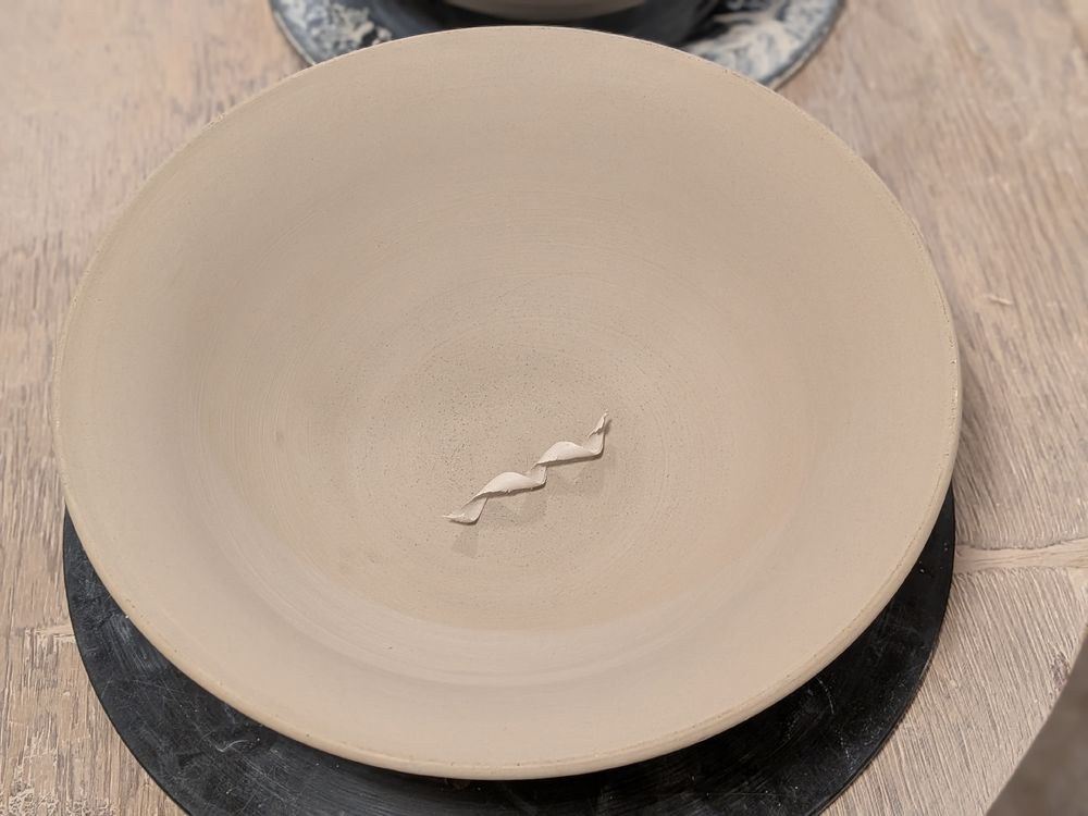 Large greenware bowl photographes from above with a clay noodle in the center. 