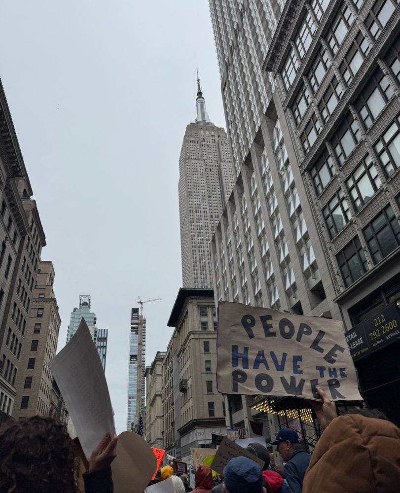 A large crowd marches past the Empire State Building in NYC. A protester’s sign reads “people have the power”