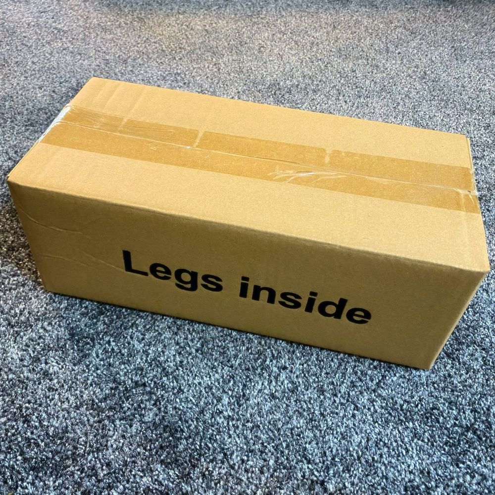 A sealed cardboard box labelled ‘legs inside’ on blue-grey carpet 