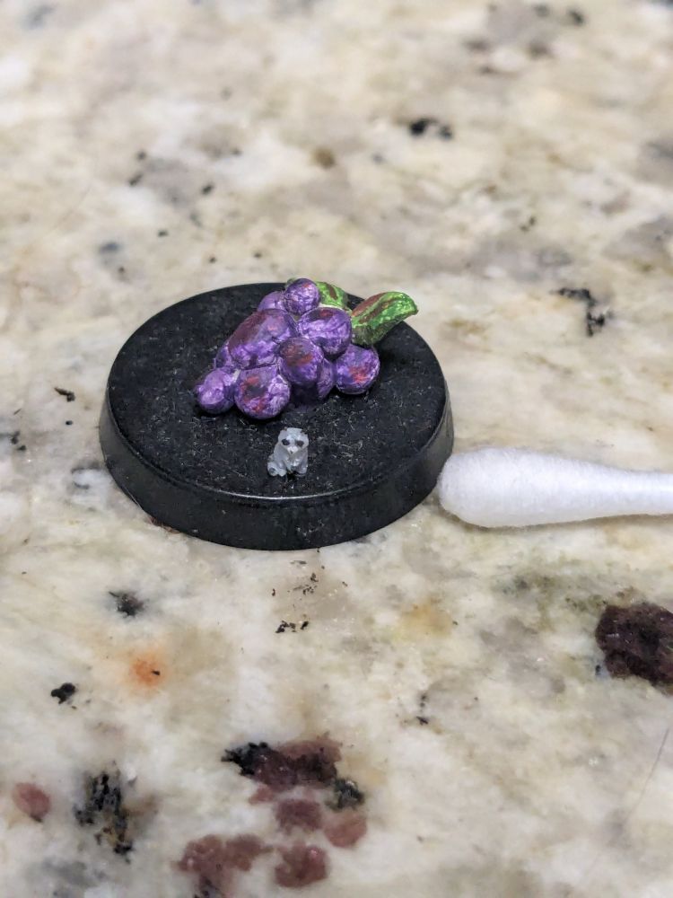 Tiny raccoon on a 25mm base with purple grapes and the end of a q-tip