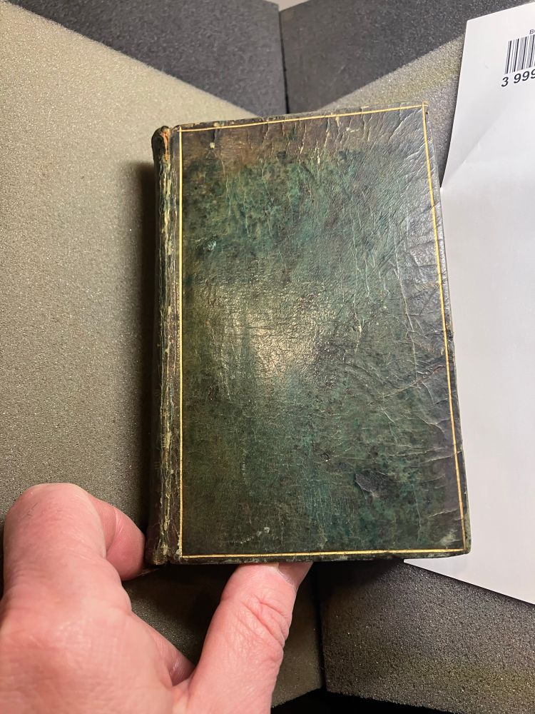 A man’s hand touches a small book, Renaissance or Restoration period, bound in green leather. 