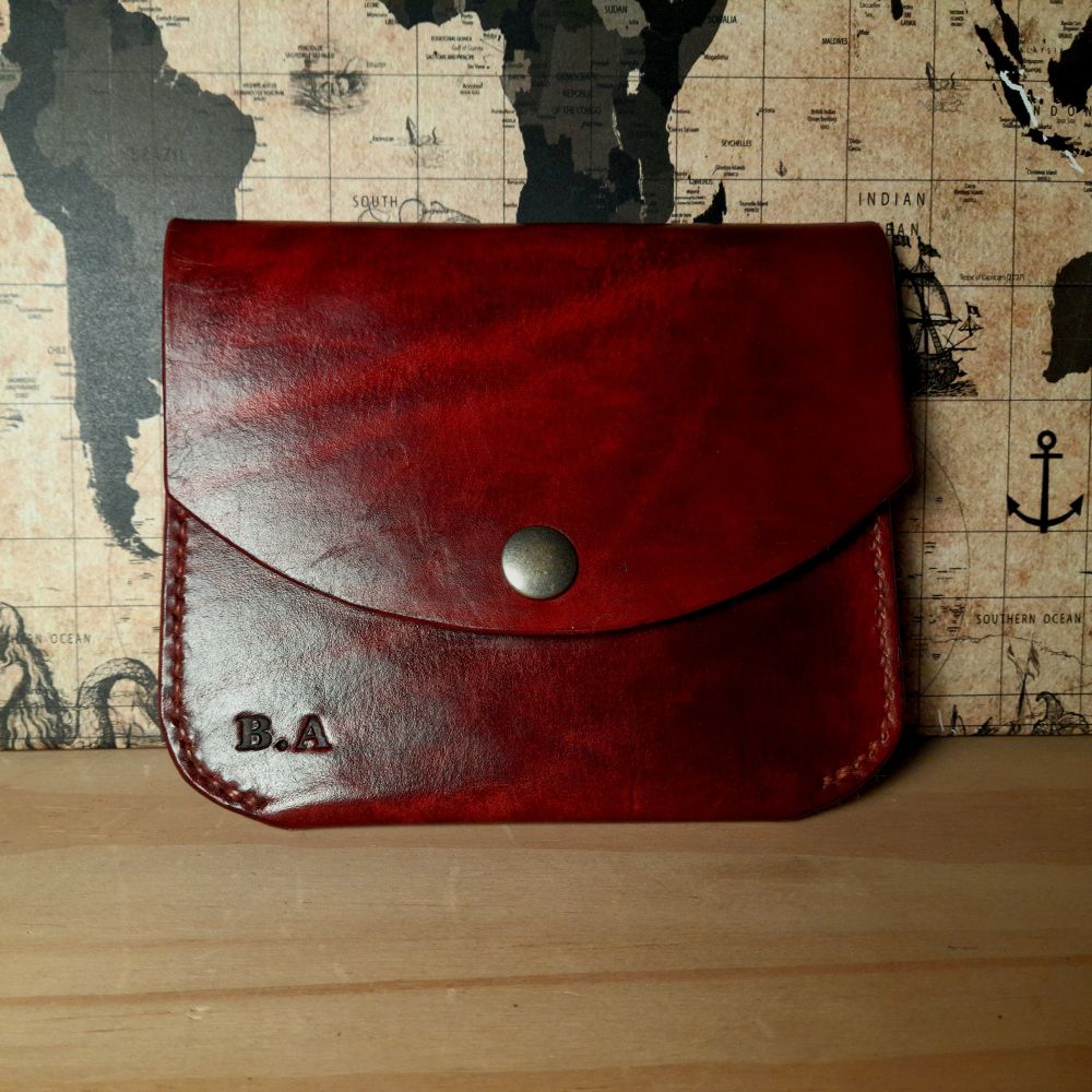 Photo d'un portefeuille en cuir marron foncé. Il est formé d'une poche à deux compartiments et se ferme avec un rabat à pression. 