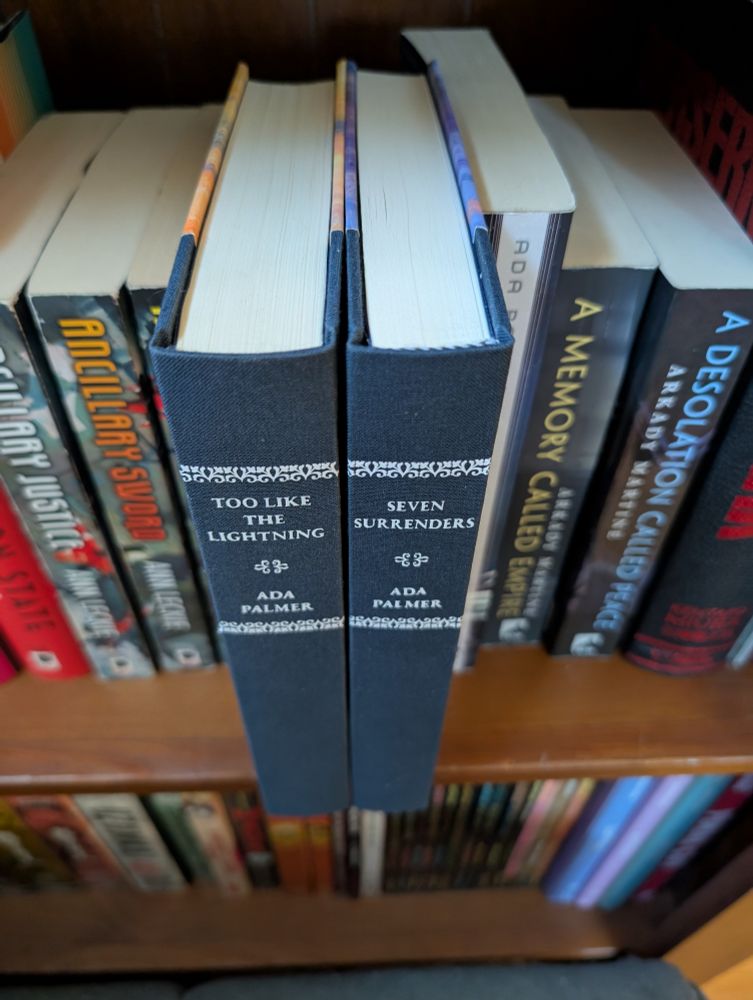 Rebound copies of Too Like The Lightning and Seven Surrenders next to each other on a shelf. The spines have navy book cloth, white text, and decorative horizontal borders.