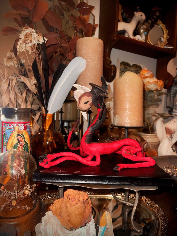 Four photographs of different angles of a first time sculpt I did of my character gren’s monster form. He’s laying with his front legs crossed and his black claws out. He’s very noodley/lanky with a curved long neck that’s encased in two tone fur of blackish brown and a creamy white. Has a light brown kitty like masked face with eyes closed. There’s 8 small wings on his head half are black-ish brown the other half the creamy white and has a massive loopy spiked tail.