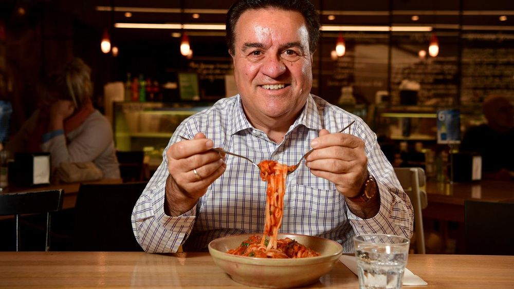 SA MP Frank Pangallo with a nice big bowl of spaghett. He is wearing a t-shirt that kind of looks like a tea towel and a big smile. Spaghett is being picked up with two forks.