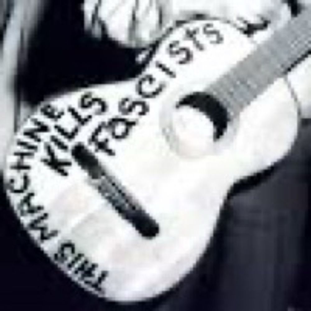 Black and white photo of Woody Guthrie’s acoustic guitar, on which is written “This Machine Kills Fascists”