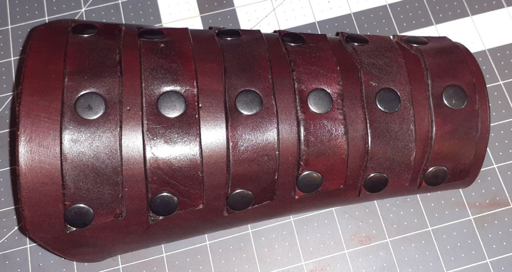 Oxblood dyed heavy veg-tan leather bracer (forearm guard) with 6 additional reinforcement straps riveted with 3 half inch black double cap rivets per strap.