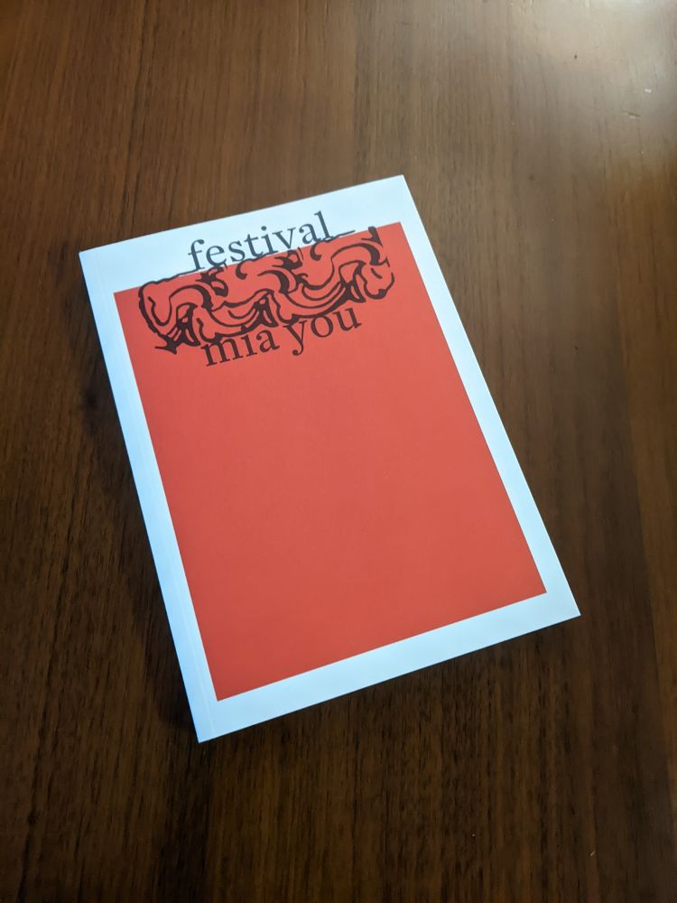 A copy of Festival by Mia You. A white-bordered paperback book with a flat field of bright red in the middle. The title, author name, and a decoration are centred near the top in black ink