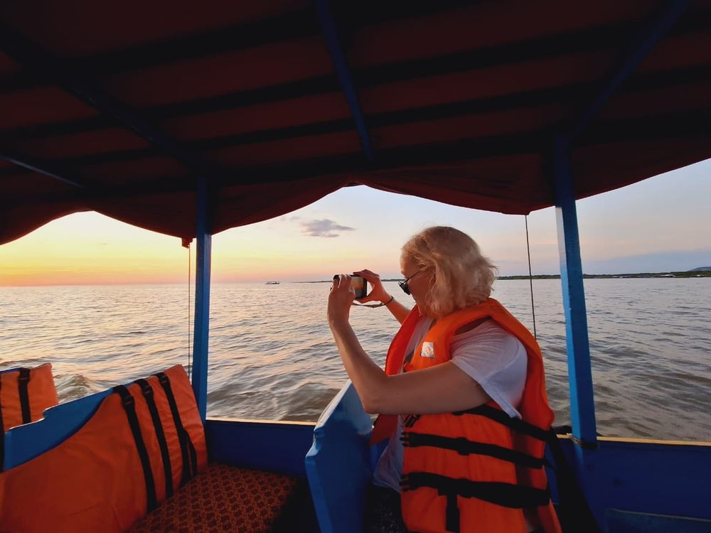 Me, on a boat, taking a photo of the sun setting over Tonle Sap Lake in Cambodia. Taken by my guide on 30th December 2023.
