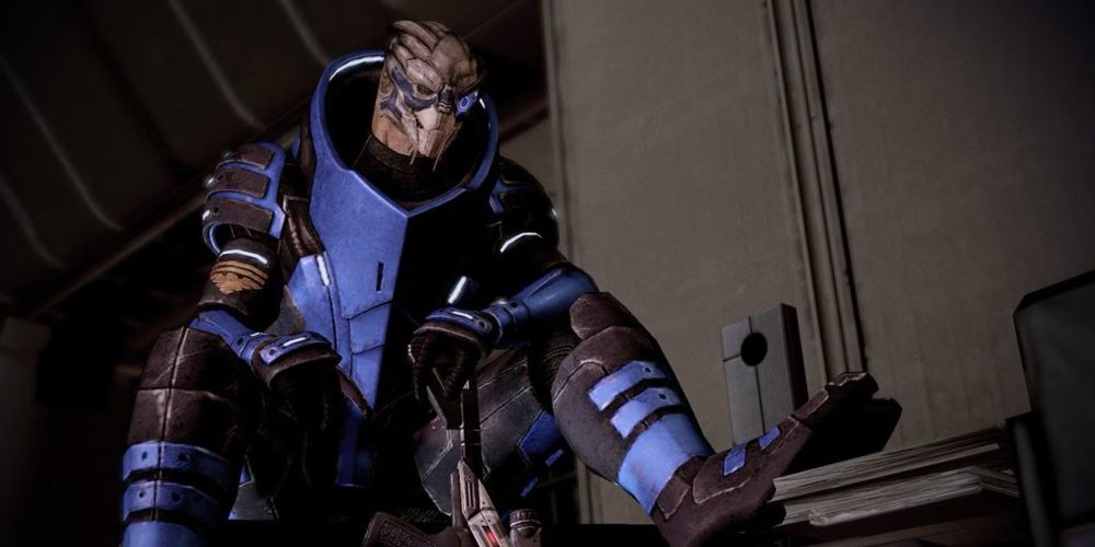 A screenshot of the video game Mass Effect 2, showing the character Garrus sitting down as he smiles towards the camera. 