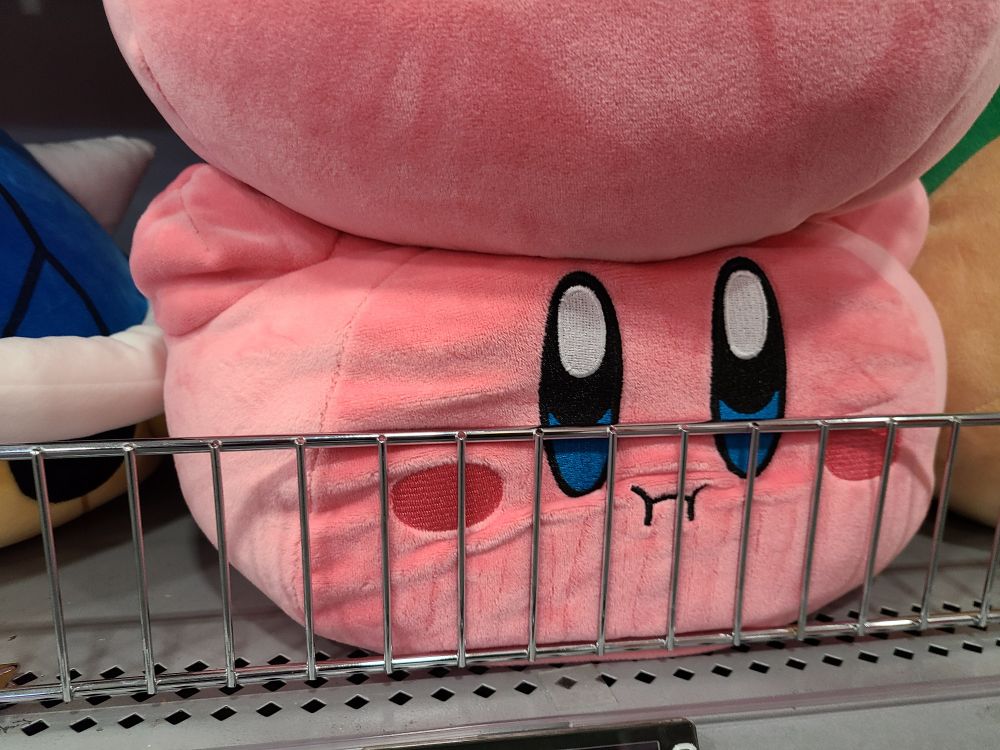 Kirby plush pressed against some bars to keep him on the shelf 