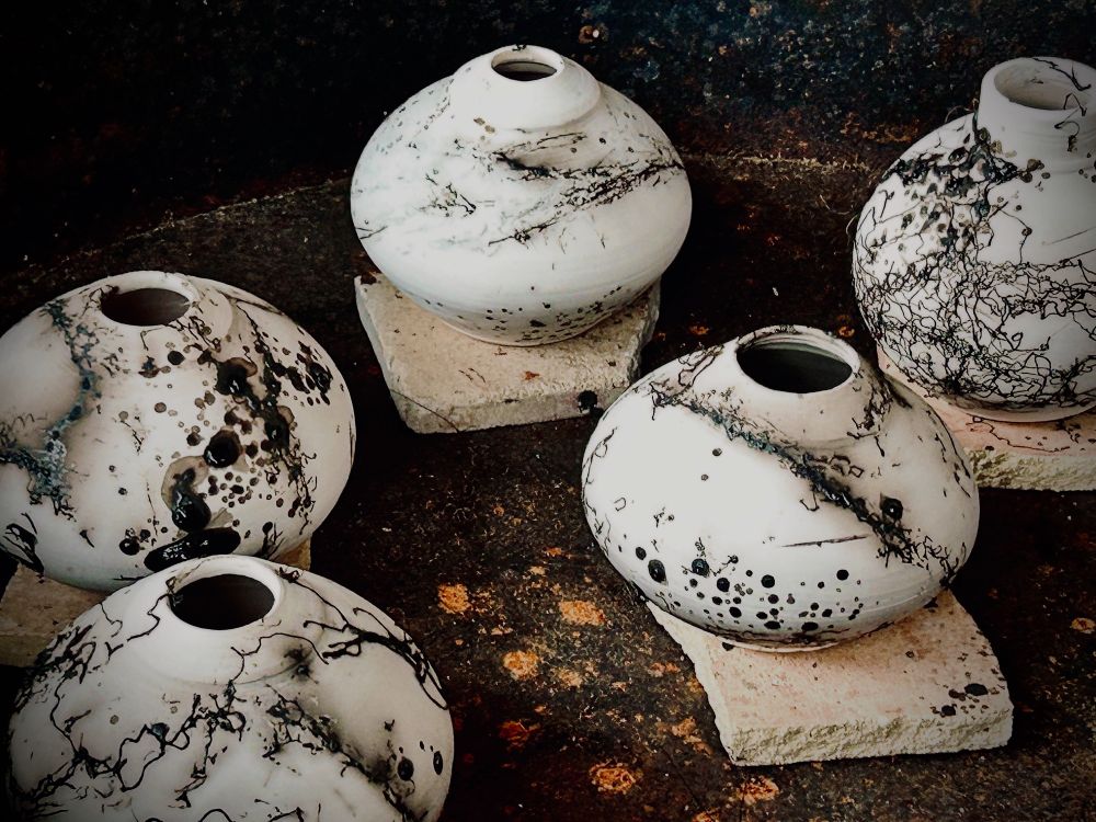 White pots fresh from the kiln with dark, splatter and twisted patterns burned onto them 
