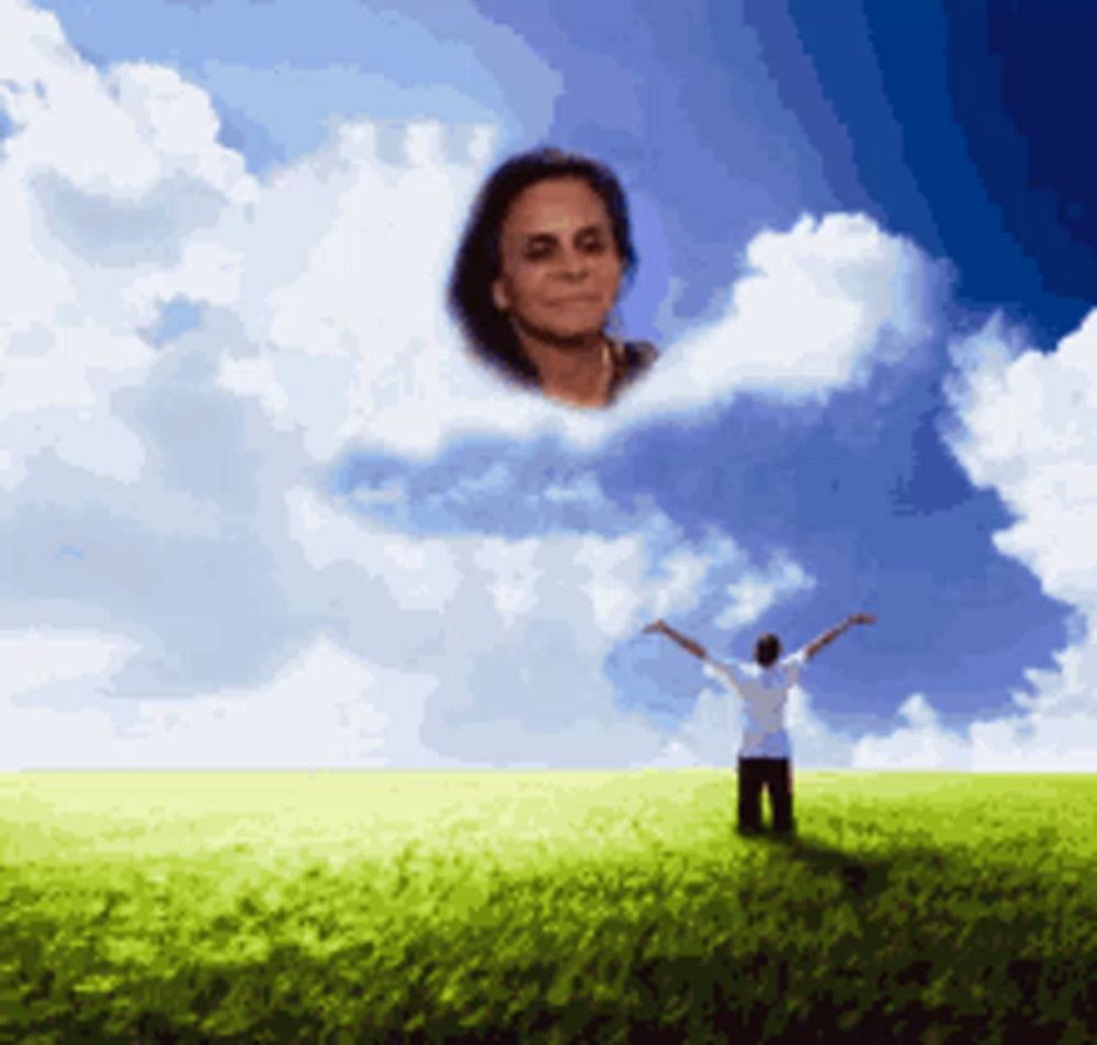 a man stands in a grassy field with his arms outstretched and a cloud with a woman 's face on it