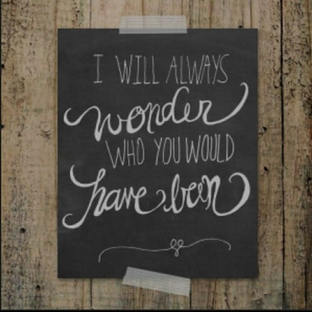 Wall of weathered boards with black chalkboard taped to it. It says, "I will always wonder who you would have been".