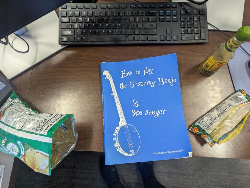 My desk with the book "How to Play the 5-string Banjo" by Pete Seeger and my lunch of a burrito and chips w/hot sauce on it.