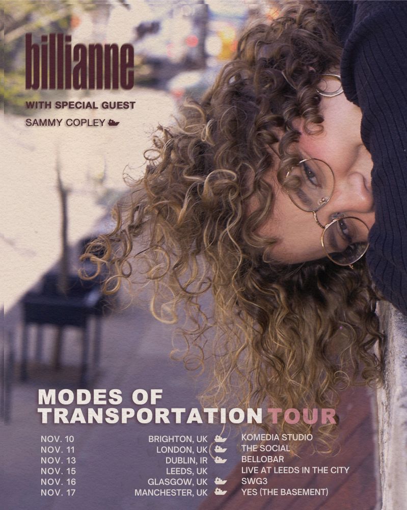 The poster for Billianne’s Modes of Transportation tour, listing the dates which feature special guest Sammy Copley. The poster is cool toned, and features Billianne to the right leaning over a wall and smiling at the camera. She has curly brown hair and is wearing glasses and a navy blue sweater.
