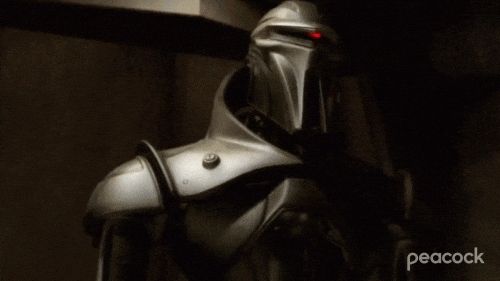 GIF from Battlestar Galactica, two different consecutive frames each show a different cylon robotic soldier in full metal suits with a red light scanning across the spot where eyes would be.