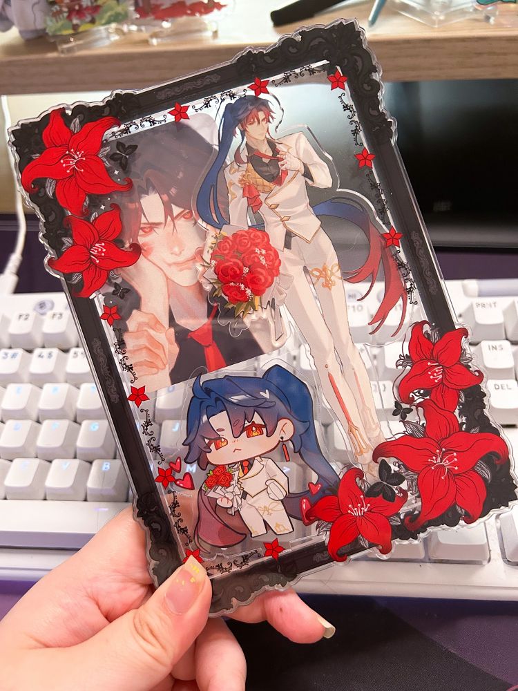 A black frame with red lillies showing a man in a white suit with long blue hair tied up with red tips holding roses