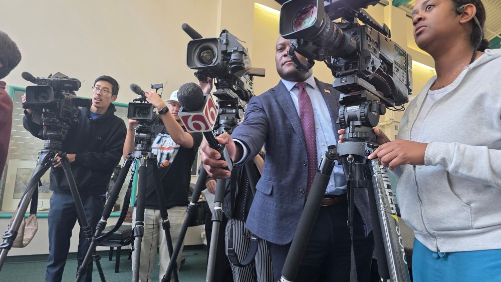 Tulsa Mayor Monroe Nichols stands in between TV reporters and their cameras while holding a microphone with the logo of KOTV Channel 6.