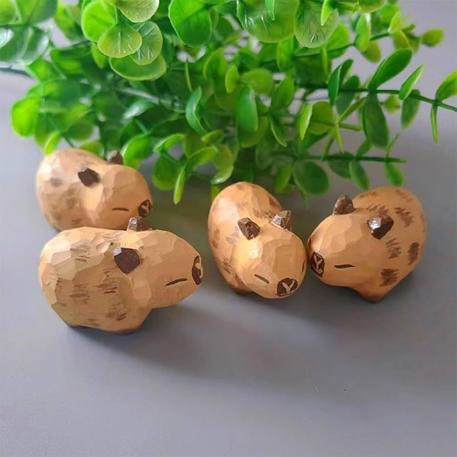 A set of four tiny wood carvings of capybaras mingling in front of a small fake plant.