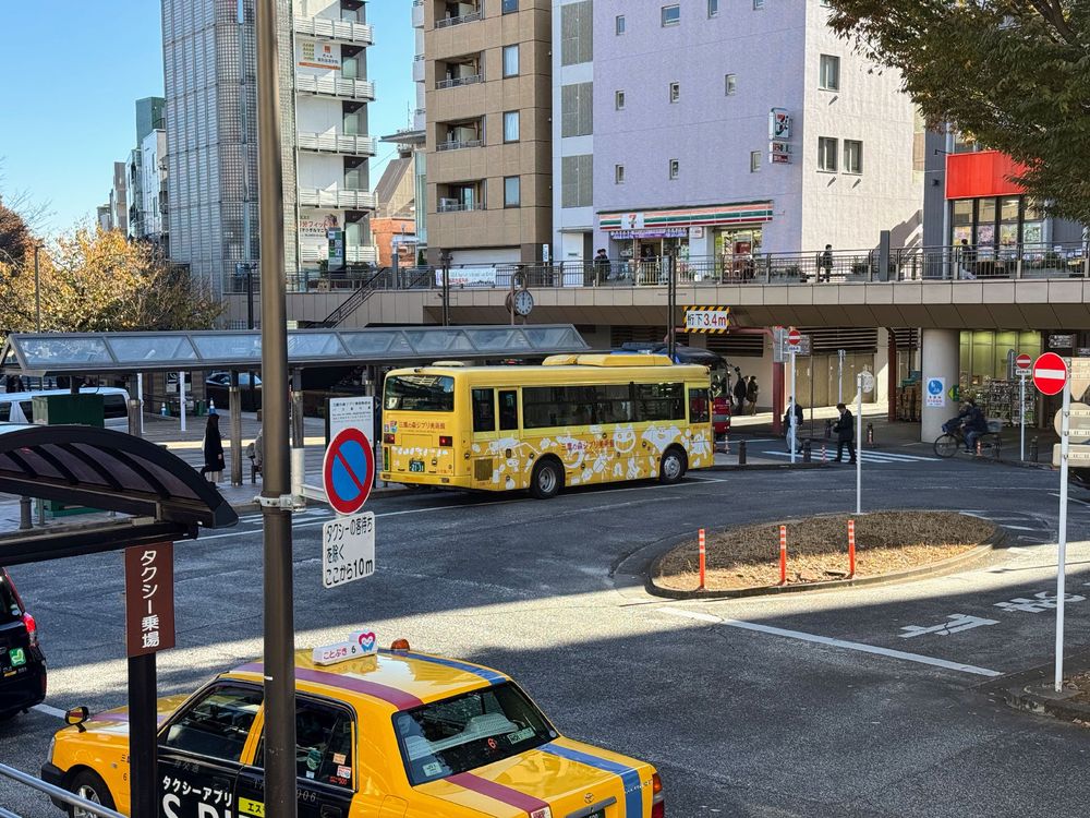 A photo of a yellow bus at a bus stop with various Studio Ghibli characters drawn on the side in white. 