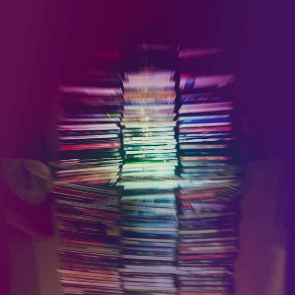 A blurred stack of CDs arranged vertically, with various colored covers partially visible. The background features a gradient of purple hues.