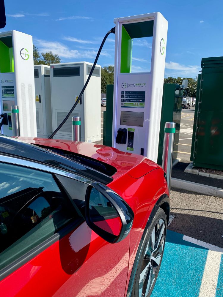 A red Renault Megane E-tech parked up and charging on a public charger on a sunny day.