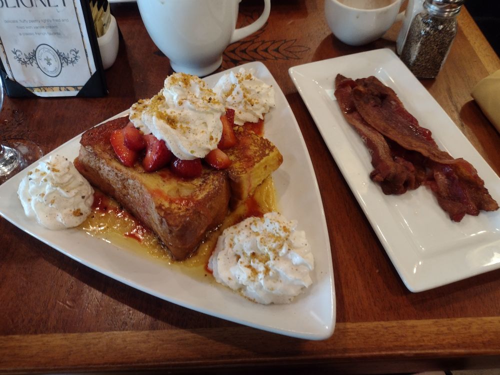 A plate of very fancy french toast with whipped cream and strawberries, and bacon