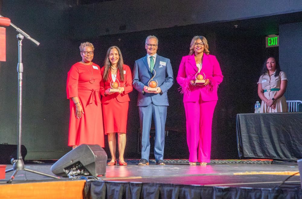 Four honorees pose on stage with their awards at the Hall of Fame event, three women and one man smiling and holding trophies.