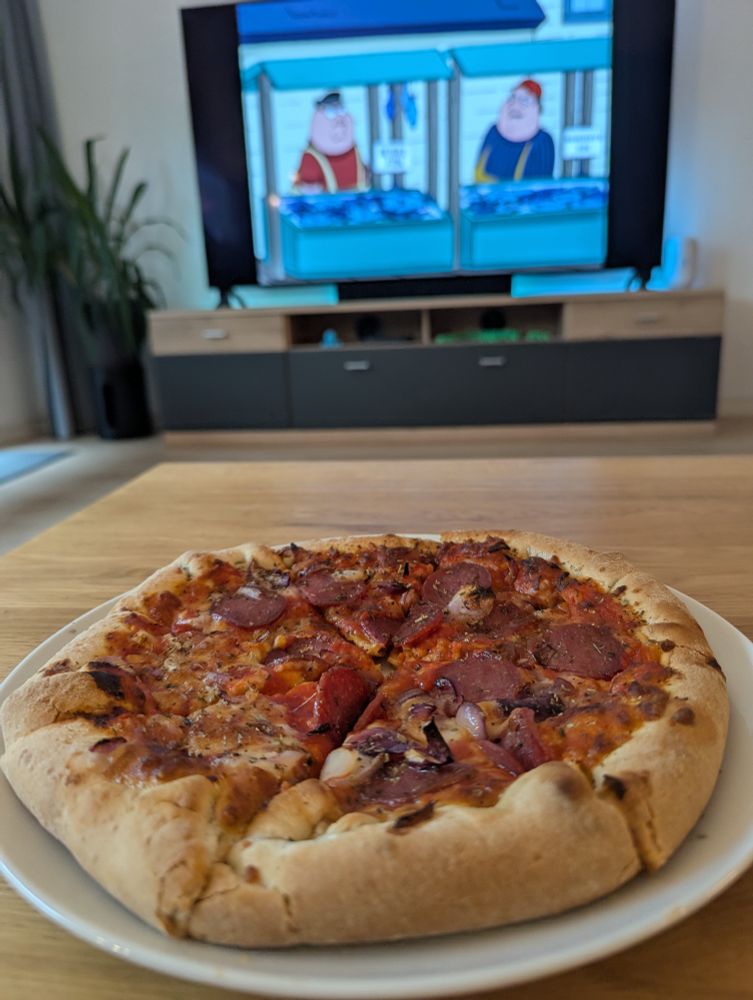 Pizza Salami auf einem Teller, im Hintergrund läuft Family Guy auf dem Fernseher 