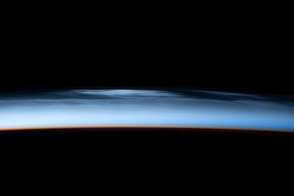 The images show a bright blueish band over a curved dark earth and under the darkness of space at top. In the upper part of the band a number of thin light streaks, mostly parallel, are visible. These are the noctilucent clouds. The other images show the same horizon and different parts of the noctilucent clouds.