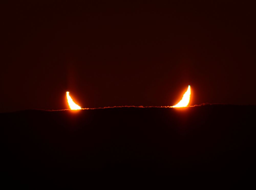 The image shows two horns of light rising from a dark horizon.