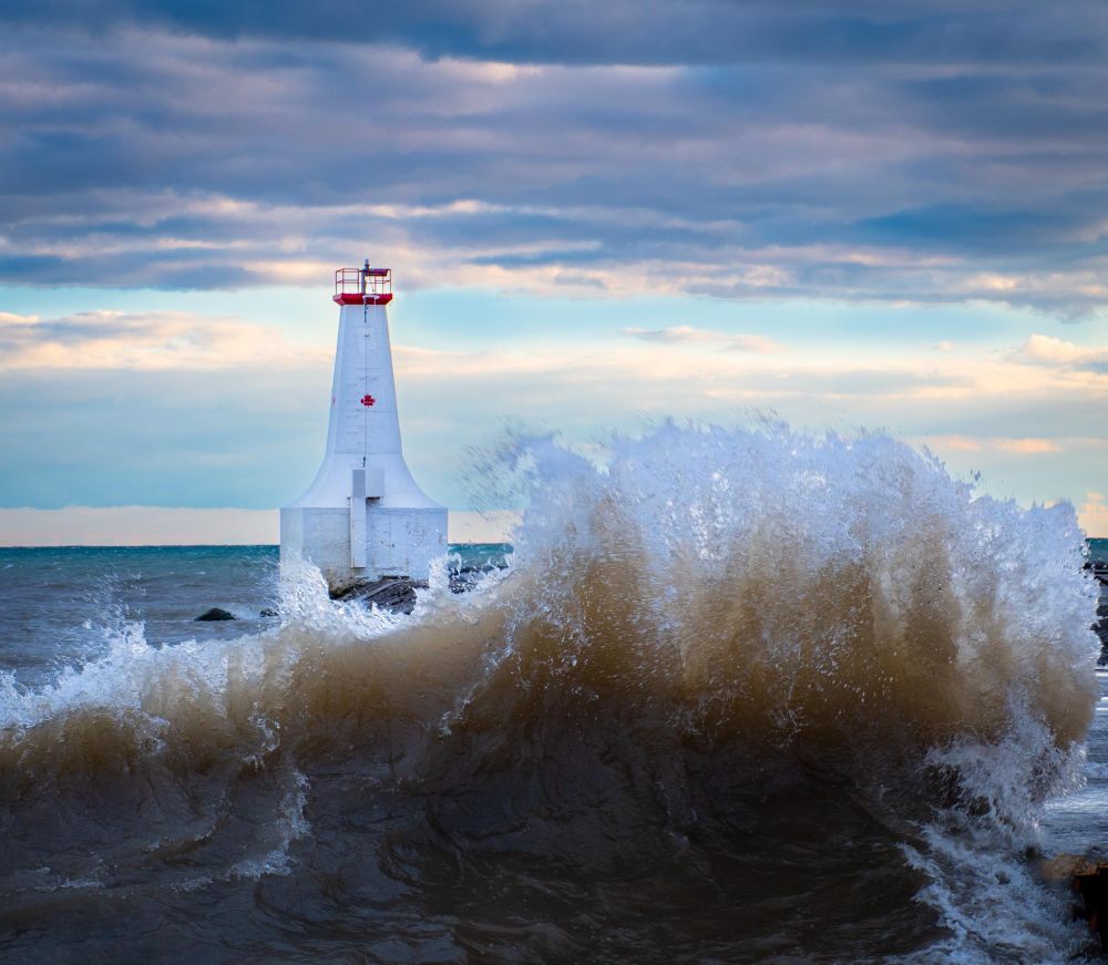 a lighthouse peeking out behind a huge wave