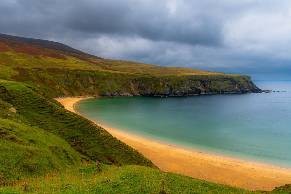 a sweeping beach at the base of cliffs with moody clouds in the sky