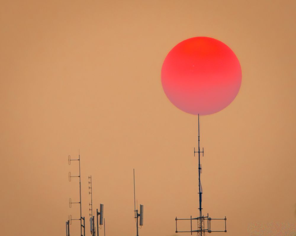 a red sun from the wildfire smoke appearing to sit on a communications tower