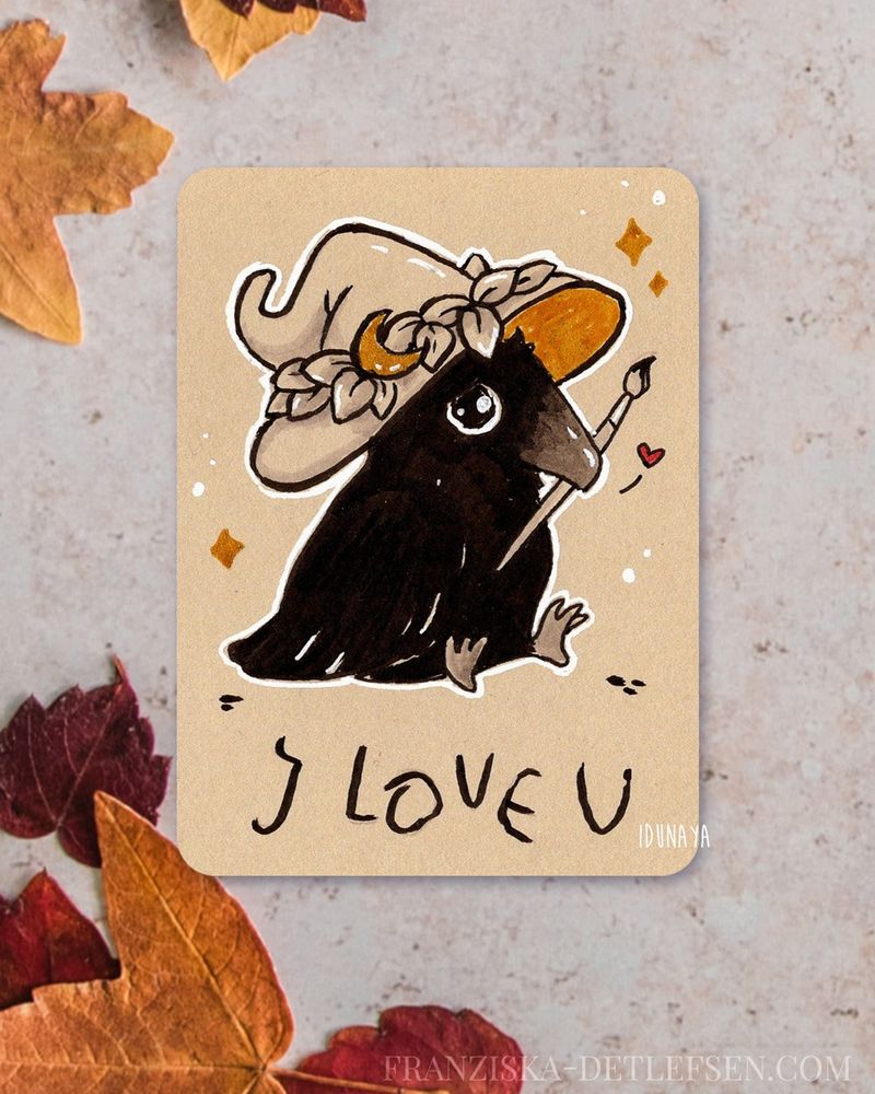 Mockup of a cardsized inkdrawing surrounded by autumn leaves. The drawing shows a cute little crow with witch hat holding a brush in it's beak. It's looking a bit sad and in shaky font the words "I love u" are written under it. 