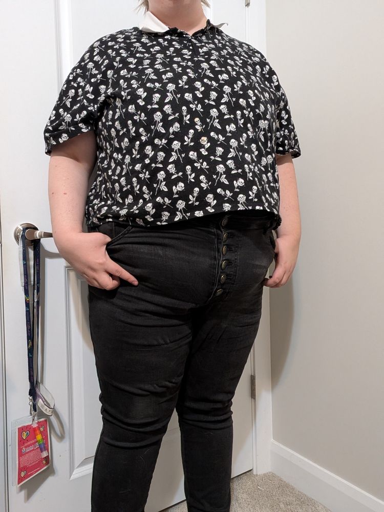 The same subject as the previous photo, but in this photo they are standing back from the camera for a full body shot with their face still out of frame. The shirt is the same as the previous photo, worn with black jeans with a button fly.