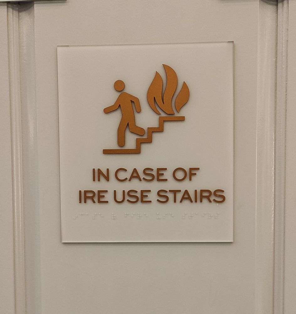 A photo of a safety placard by a hotel elevator that reads "In case of ire use stairs".
