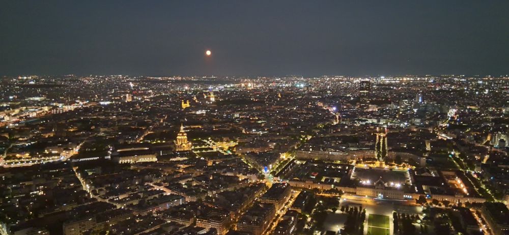 Paris from the top of the Eiffel Tower, with a near full moon in the sky.