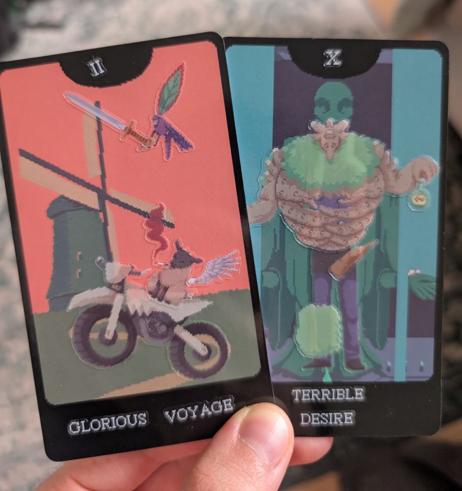 Dos cartas hechas con el juego físico de pegatinas de the cosmic wheel sisterhood. En una, titulada glorious voyage, una cabra fumona y alada viaja en moto con su amigo el loro espadachín. En la otra, llamada terrible desire un golem barman te sirve veneno con una rocosa erección 