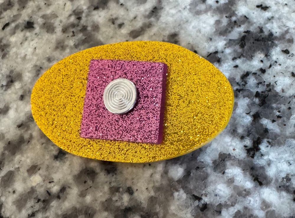 Glittery yellow and pink perspex eye-shaped brooch with a silver rivet as the pupil