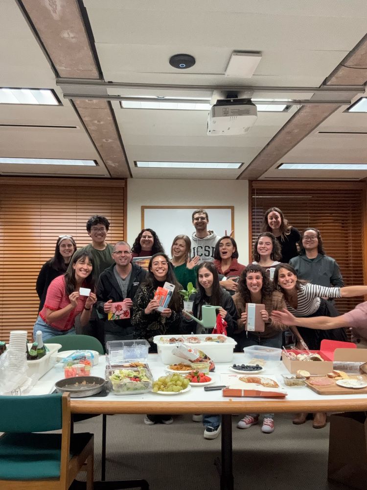 The Allen lab shows off their white elephant gifts behind a table of food 