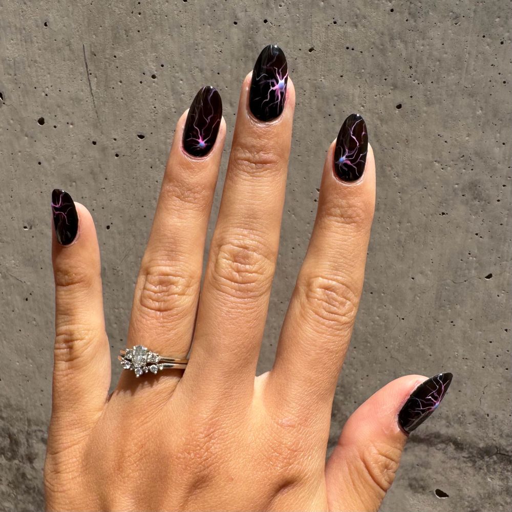 Hand against concrete wall. The nails are painted black with pink astrocytes (a star shaped brain cell) with a blue DAPI nucleus 